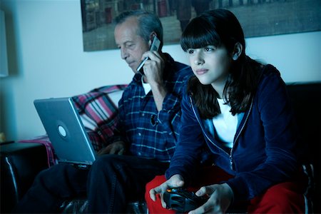 Grandfather works on laptop while granddaughter plays video game Stock Photo - Premium Royalty-Free, Code: 644-01436485