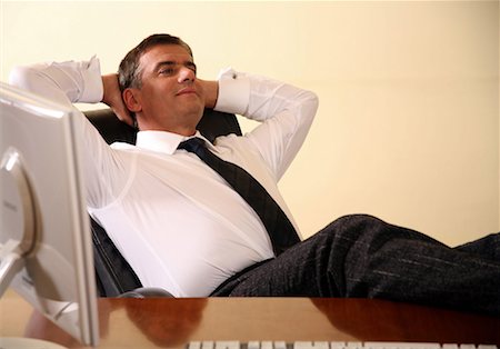 Businessman sitting at his desk with hands behind his head Stock Photo - Premium Royalty-Free, Code: 644-01436488