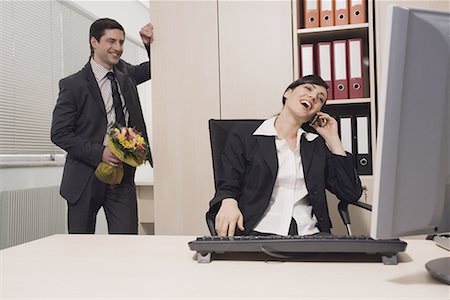 Male office worker about to surprise female colleague with flowers Stock Photo - Premium Royalty-Free, Code: 644-01630897