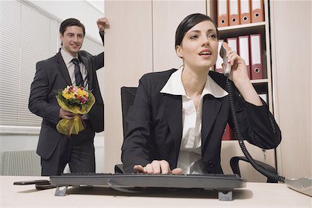 Male office worker about to surprise female colleague with flowers Stock Photo - Premium Royalty-Free, Code: 644-01630900