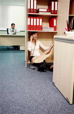 Office worker on the phone hiding from manager Stock Photo - Premium Royalty-Free, Code: 644-01630913