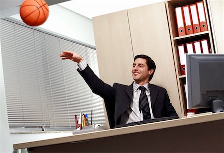 Office worker at desk playing with a basketball Stock Photo - Premium Royalty-Free, Code: 644-01630932