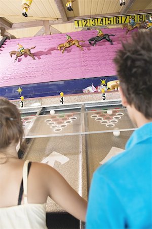 Teenage couple playing horse racing game in amusement park Stock Photo - Premium Royalty-Free, Code: 644-01825505