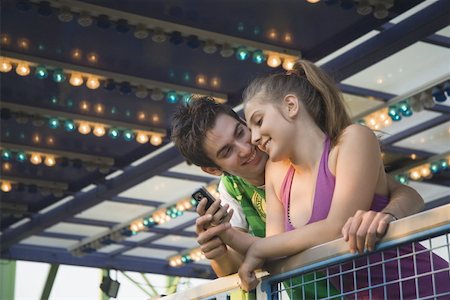 Teenage couple with cell phone at amusement park ride Stock Photo - Premium Royalty-Free, Code: 644-01825627