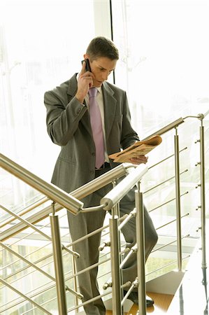 Businessman with financial newspaper on staircase talking on cell phone Stock Photo - Premium Royalty-Free, Code: 644-02923201
