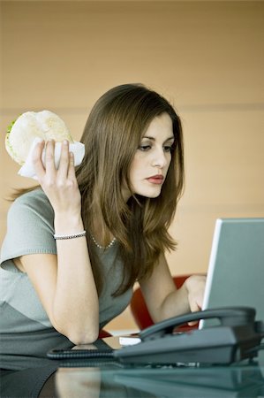 snacking desk - Businesswoman eating pita sandwich at laptop Stock Photo - Premium Royalty-Free, Code: 644-02923291