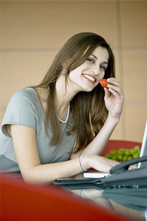 Businesswoman eating a strawberry at laptop Stock Photo - Premium Royalty-Free, Code: 644-02923293