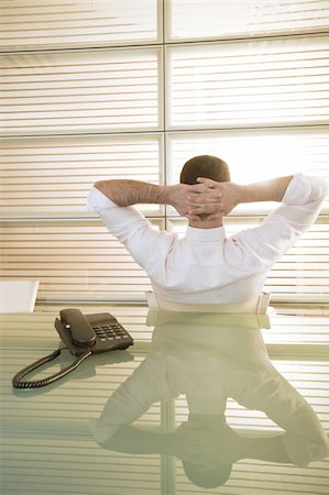 Back view of businessman in office with hands behind head Stock Photo - Premium Royalty-Free, Code: 644-02923324