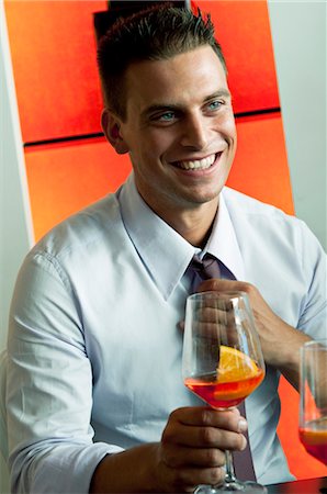 Young man in business attire with glass of orange wine adjusting tie Stock Photo - Premium Royalty-Free, Code: 644-03405264