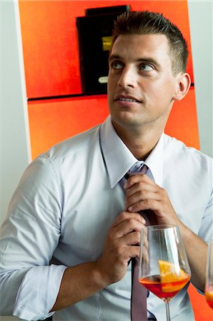Young man in business attire with glass of orange wine adjusting tie Stock Photo - Premium Royalty-Free, Code: 644-03405266