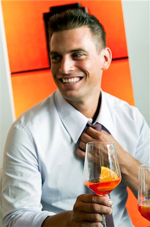 Young man in business attire with glass of orange wine adjusting tie Stock Photo - Premium Royalty-Free, Code: 644-03405263