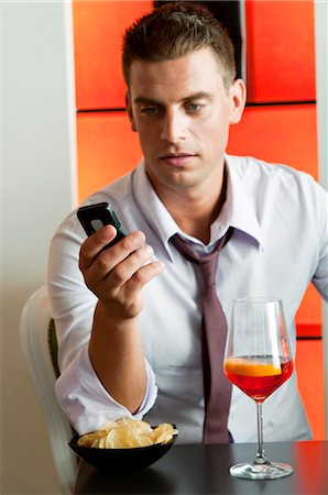 simsearch:644-03405258,k - Jeune homme assis avec un verre de vin orange et téléphone mobile Photographie de stock - Premium Libres de Droits, Code: 644-03405277