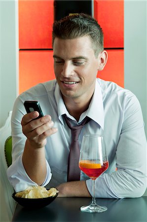 simsearch:644-03405258,k - Jeune homme assis avec un verre de vin orange et téléphone mobile Photographie de stock - Premium Libres de Droits, Code: 644-03405278