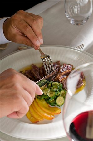 Closeup of young man's hands with knife and fork at his plate Stock Photo - Premium Royalty-Free, Code: 644-03405327