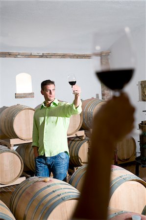 Young woman's hand holding glass of red wine with young man in background holding up his wineglass Stock Photo - Premium Royalty-Free, Code: 644-03405506