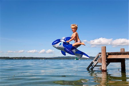 Boy jumping into lake with toy whale Stock Photo - Premium Royalty-Free, Code: 649-05556079