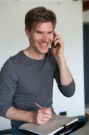 Homme souriant sur téléphone cellulaire, prise de notes Photographie de stock - Premium Libres de Droits, Code: 649-05801085