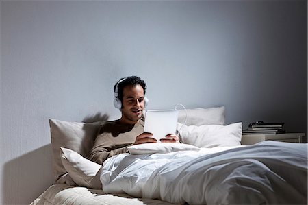 Man using tablet computer in bed Stock Photo - Premium Royalty-Free, Code: 649-05820811