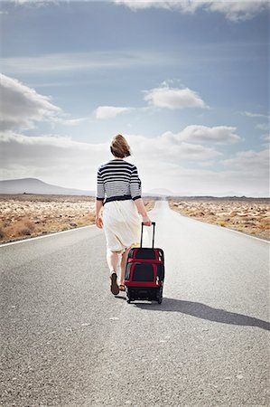 Woman rolling luggage on rural road Stock Photo - Premium Royalty-Free, Code: 649-05950791