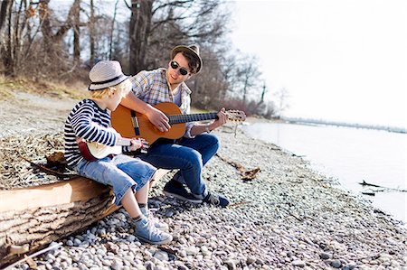 people sitting playing a guitar - Father and son playing guitars by creek Stock Photo - Premium Royalty-Free, Code: 649-06040818