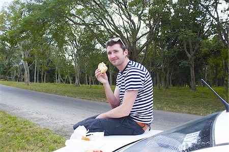 person eating a hamburger - Man eating sandwich on trunk of car Stock Photo - Premium Royalty-Free, Code: 649-06113225