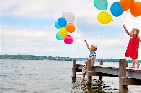 Children holding balloons on wooden pier Stock Photo - Premium Royalty-Free, Code: 649-06305414