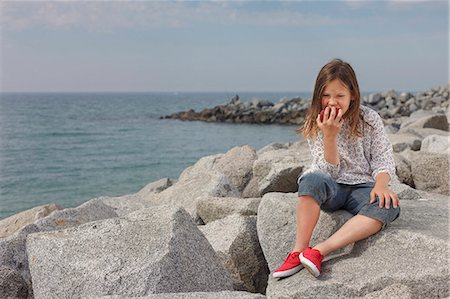 Girl eating apple on rocky beach Stock Photo - Premium Royalty-Free, Code: 649-06305492