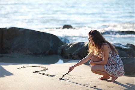 female crouching pic - Woman drawing question mark in sand Stock Photo - Premium Royalty-Free, Code: 649-06432361