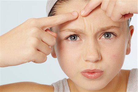 frustrated child white background - Girl squeezing spot on her face Stock Photo - Premium Royalty-Free, Code: 649-06533064