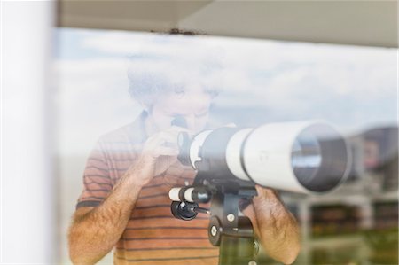 Man using telescope at window Stock Photo - Premium Royalty-Free, Code: 649-06717019