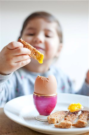 Girl dipping toast into egg at breakfast Stock Photo - Premium Royalty-Free, Code: 649-06717462
