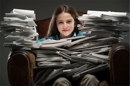 Girl sitting in leather armchair with piles of books, smiling Stock Photo - Premium Royalty-Free, Code: 649-06812234