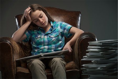 Girl sitting in leather armchair with piles of books Stock Photo - Premium Royalty-Free, Code: 649-06812236