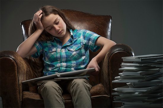 Girl sitting in leather armchair with piles of books Stock Photo - Premium Royalty-Free, Image code: 649-06812236