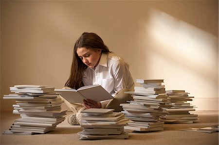 Girl sitting on floor reading surrounded by piles of books Foto de stock - Sin royalties Premium, Código: 649-06812239