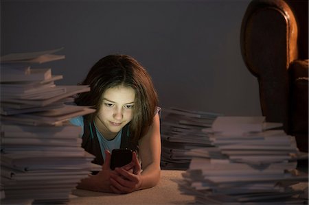 Girl lying on front using cell smartphone surrounded by books Stock Photo - Premium Royalty-Free, Code: 649-06812232