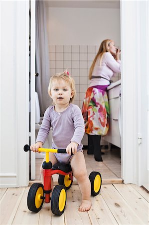 family with toddler - Toddler girl playing on tricycle, mother in background Stock Photo - Premium Royalty-Free, Code: 649-06812252