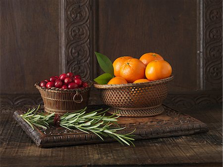 Ingredients to create Clementine and Cranberry Lamb Rack. Clementines in woven wooden bowl, cranberries in small wooden bowl and sprigs of rosemary Fotografie stock - Premium Royalty-Free, Codice: 649-06812289