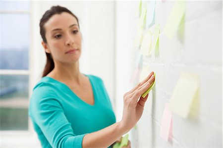 Mid adult woman sticking adhesive notes to wall Stock Photo - Premium Royalty-Free, Code: 649-06812631