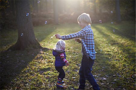 Boy blowing bubbles in forest for toddler girl Stock Photo - Premium Royalty-Free, Code: 649-06812979