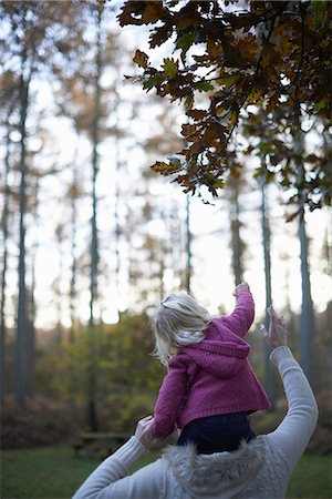 Girl sitting on mother's shoulders reaching for leaf Stock Photo - Premium Royalty-Free, Code: 649-06812995