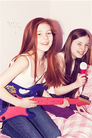Two girls playing guitar and singing into microphone in bedroom Stock Photo - Premium Royalty-Free, Code: 649-06829588
