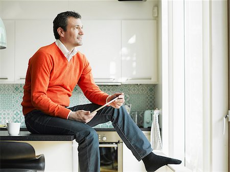suéters - Mature man holding tablet and sitting on kitchen worktop Foto de stock - Sin royalties Premium, Código: 649-06829607