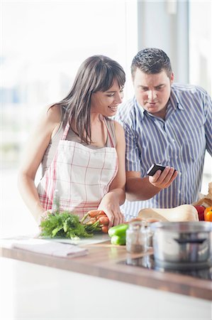 Couple looking at smartphone whilst preparing food Fotografie stock - Premium Royalty-Free, Codice: 649-06844143
