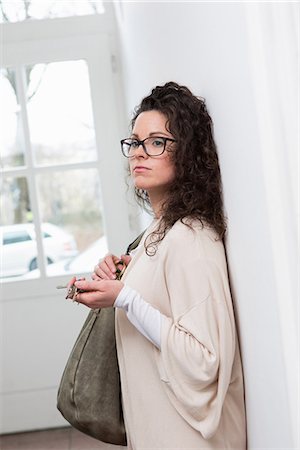 Woman leaning against wall in hallway holding keys and handbag Stock Photo - Premium Royalty-Free, Code: 649-06844822