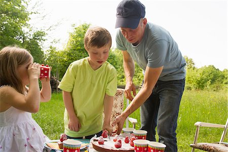 Father with two children cutting birthday cake outdoors Stock Photo - Premium Royalty-Free, Code: 649-06845260
