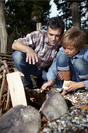 father helping boy image - Father and son lighting fire outdoors Stock Photo - Premium Royalty-Free, Code: 649-06943766