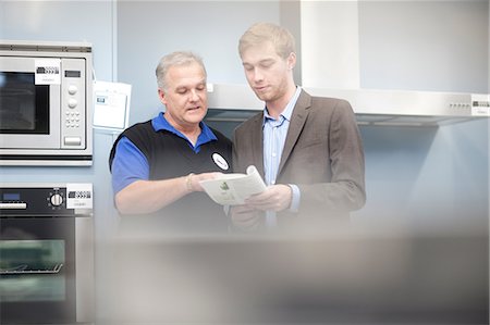 sales associate talking with customer - Young man looking at appliance brochure in showroom Stock Photo - Premium Royalty-Free, Code: 649-07064074