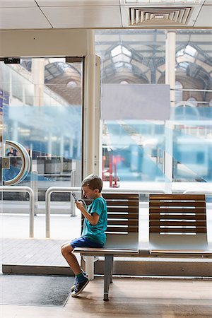 simsearch:614-06044044,k - Young boy in train station waiting room playing electronic game Foto de stock - Sin royalties Premium, Código: 649-07064450