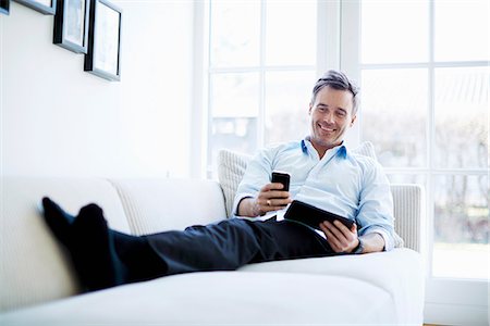 smile relaxed - Man relaxing on sofa using digital tablet and smartphone Stock Photo - Premium Royalty-Free, Code: 649-07064534